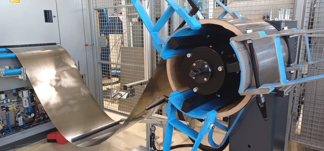 Breites Metallband wird von einer blauen Haspel in eine Laserschneidanlage geführt und zeigt den automatisierten Prozess beim Laserschneiden vom Coil