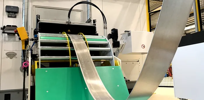 Thin strip material runs through a coil processing system and shows the automatic material feed